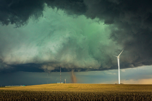 Wray CO EF3 Tornado forming under a spectacular supercell thunderstorm over harvested grain stalks in agricultural field: wind turbine in foreground, also communications towers and antenna.