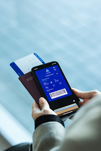 Passenger holding smartphone checking travel information on electronic boarding pass before flying. Traveler using digital boarding pass for air travel.