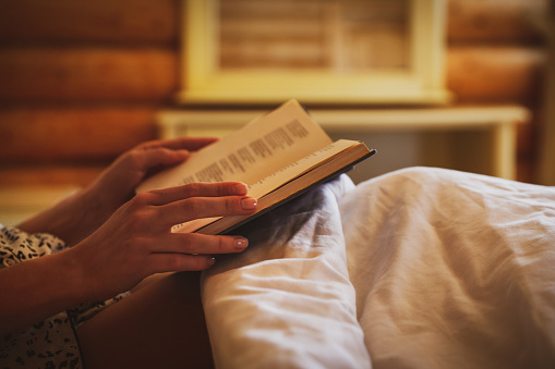 Woman reading book in bed at home, closeup