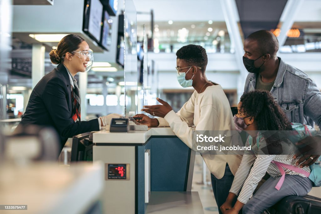 African family at airport check-in desk with face masks Passengers standing at check-in counter with airport staff during pandemic. African family in covid-19 outbreak at check-in desk of airport. Airport Stock Photo