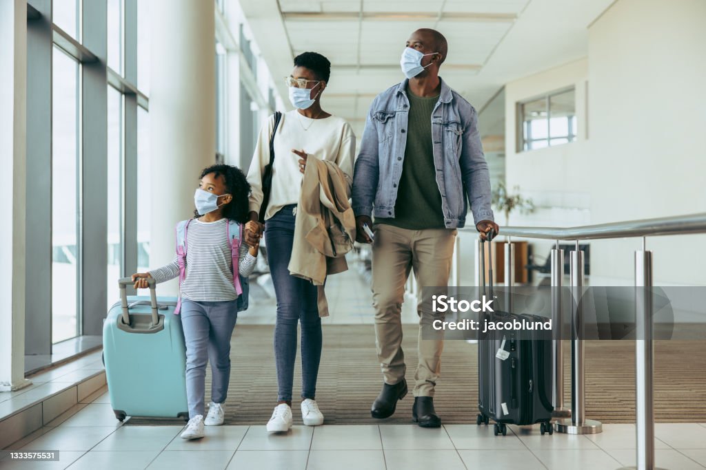 Tourist family walking through passageway in airport Tourist family walking through passageway in airport. Young girl with family in face masks walking with luggage in airport corridor. Travel Stock Photo