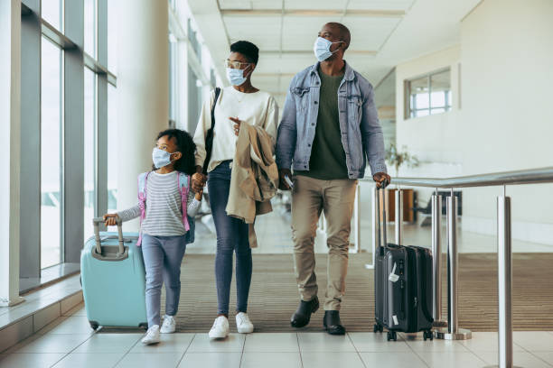 Tourist family walking through passageway in airport Tourist family walking through passageway in airport. Young girl with family in face masks walking with luggage in airport corridor. travel destinations family stock pictures, royalty-free photos & images