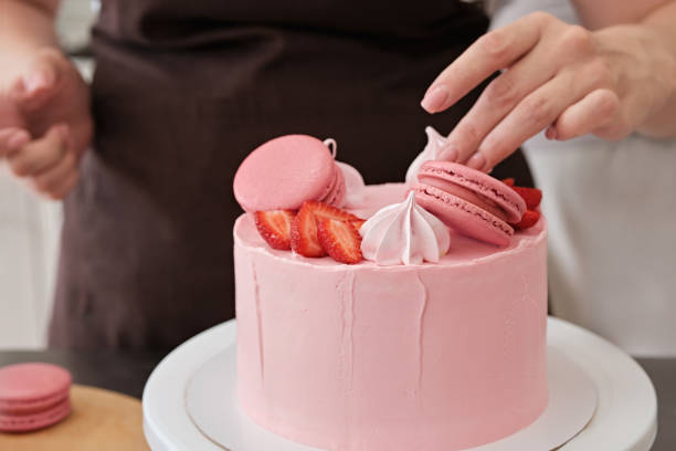 istock Woman pastry chef decorates pink cake with macaroons and berries, close-up. Cake making process, Selective focus 1333575664