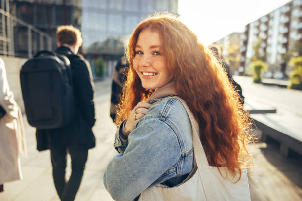 Beautiful student walking and smiling back at camera Beautiful young woman going for college. Cheerful student walking toward her class and looking behind. looking over shoulder stock pictures, royalty-free photos & images