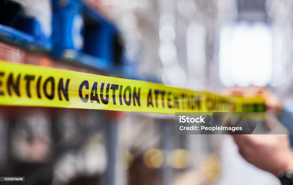 Shot of a unrecognizable man putting up tape in a warehouse Don't forget to read the sign Safety Stock Photo