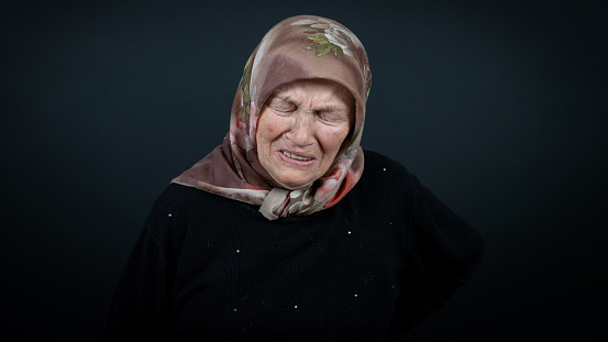 Portrait of a Turkish senior muslim woman with black background. She is sad, unhappy and crying.