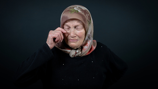 Portrait of a Turkish senior muslim woman with black background. She is sad, unhappy and crying.