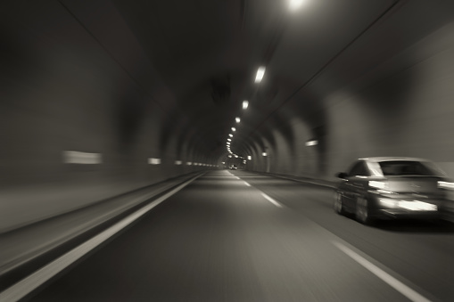 Car speeding through motorway tunnel motion blur. Black and white tint long exposure.