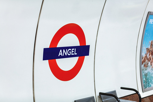 London, England - 27 June 2021: Underground tube metro with motion moving red subway train in Angel sign nobody on platform station