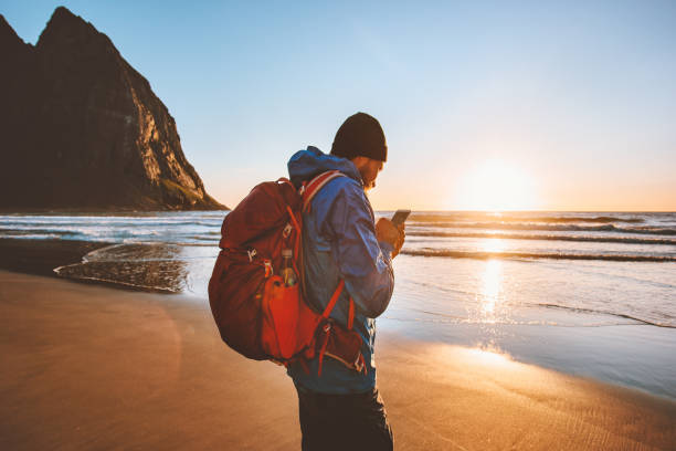 istock Man backpacker using smartphone gps navigation application outdoor walking on Kvalvika beach in Norway sunset ocean landscape 1333581342