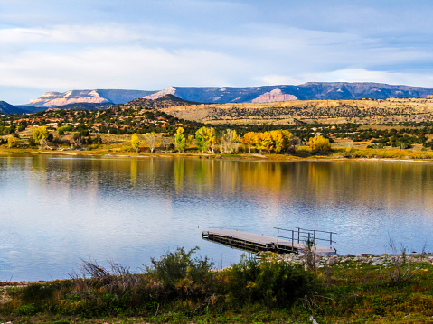 Morning view over the wide hollow reservoir just outside the town of Escalante, Utah, USA, with Fremon's Cottonwood in fall foliage, on the opposite bank reflecting in the water.