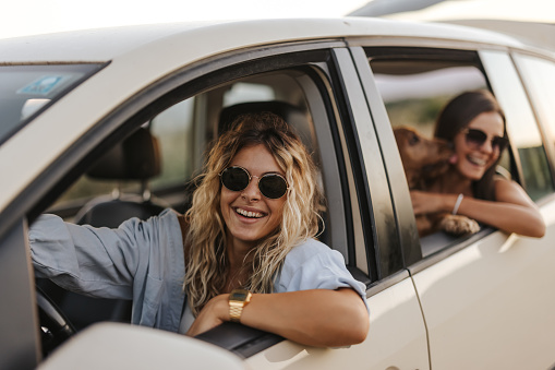 Two young cheerful female friends with cocker spaniel dog enjoying summer road trip