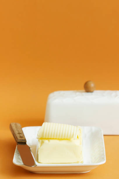 um pedaço de manteiga no prato de manteiga e uma faca em um fundo colorido. - butter dairy product butter dish milk - fotografias e filmes do acervo