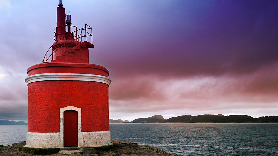 Punta Robaleira beautiful red lighthouse, Rias Baixas, Pontevedra province, Galicia, Spain. Cíes islands and sunset  in the background.