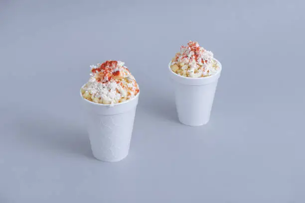 Photo of Mexican snack, two trolley, prepared esquite, corn in a cup, with chili powder on orange background