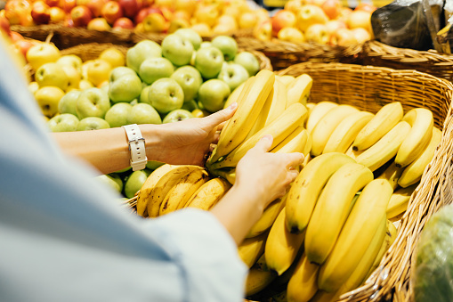 Shopping for groceries, close-up female hands take fresh bananas from store shelf.