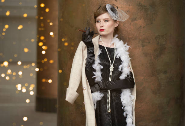 A young beautiful woman in a historical costume of the 20s or 30s of the XX century with a boa and a mouthpiece against the background of lights looks away A young beautiful woman in a historical costume of the 20s or 30s of the XX century with a boa and a mouthpiece against the background of lights looks away. High quality photo 1930s style stock pictures, royalty-free photos & images