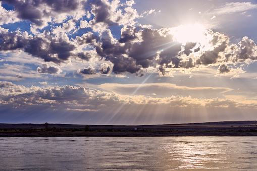 dramatic clouds and sunrise over a steppe river with a calm current. Nature landscape