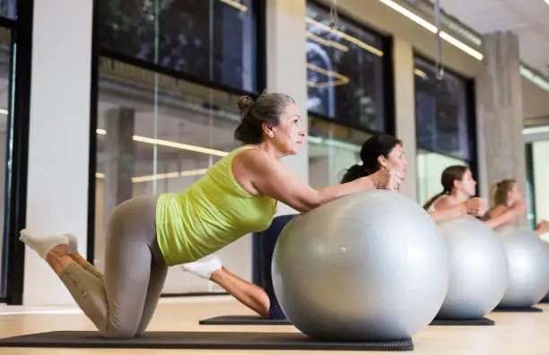 Women doing roll-out exercise with stability balls in fitness room