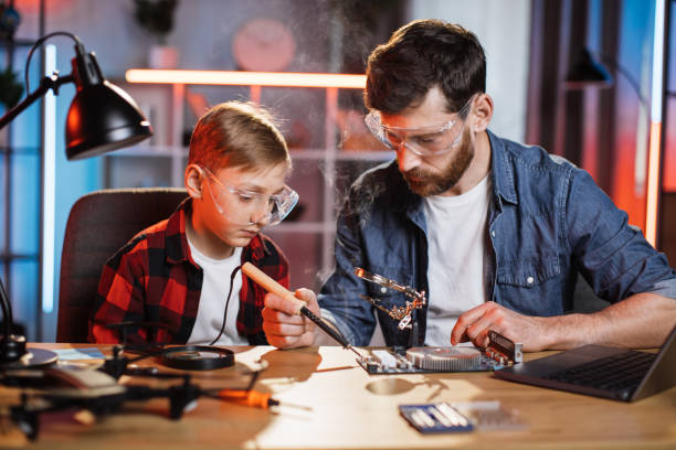 istock Bearded man and little boy soldering display card 1333613300