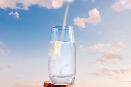 Close-up collagen spoon and glass water drink blue sky background. Sustainability, beauty and healthy living concept