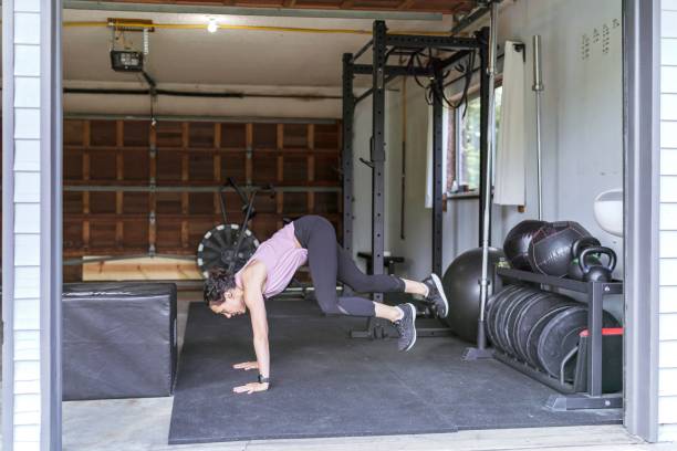 Strong Ethnic Woman Doing Cardio In Her Home Gym A gorgeous thirty something ethnic woman is exercising inside her home gym. She's wearing a purple tank top and doing burpee box jumps. burpee stock pictures, royalty-free photos & images