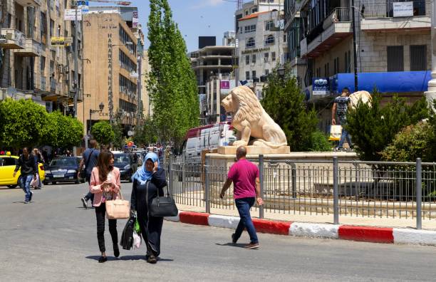On the main square of Al-Manara in Ramallah, Palestine Ramallah, Palestine, May 4, 2019: The people walk through the Al-Manara Square in the center of Ramallah. This circular square is dominated by a monument with stone lions who are described as a traditional symbol symbols of bravery, power and pride. city street street corner tree stock pictures, royalty-free photos & images