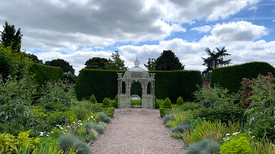 A stunning Georgian gazebo in the beautiful grounds of Arley Hall Cheshire England.Not hard to imagine a character from a Jane Austin novel enjoying a delightful conversation with fellow guests at a stately house on a warm sunny afternoon down amongst the flowers.Just before it starts raining!