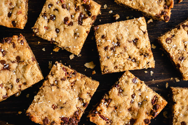 Brown Butter Bourbon Pecan Chocolate Chunk Blondies Garnished with Flaky Sea Salt Blondies cut into squares and served on a dark wood cutting board blondy stock pictures, royalty-free photos & images