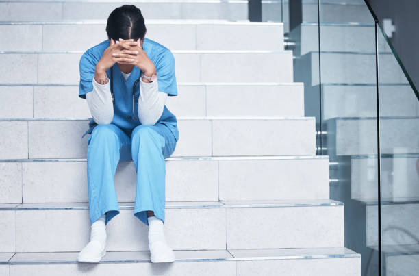 Shot of a female nurse looking stressed while sitting on a staircase Treating sick people isn't easy and losing them is even harder mental burnout photos stock pictures, royalty-free photos & images