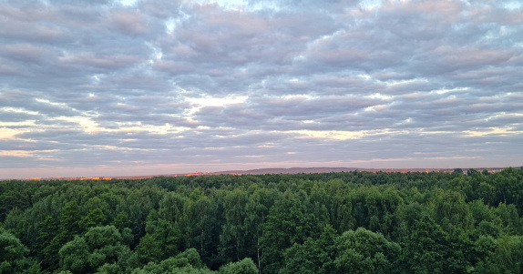 orange-purple sky with clouds at sunset and dark green forest below