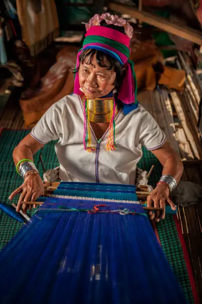 Long-neck woman from Padaung (Karen) tribe weaving on a loom, Mae Hong Son Province in Northern Thailand.