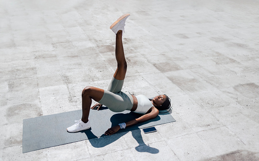 portrait of young african american woman doing bridge with single leg up on grey yoga mat