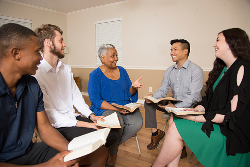 Multi Ethnic Group of friends meet for a Bible Study.  Group includes a teenager, young adults, mid-adult and senior adult.