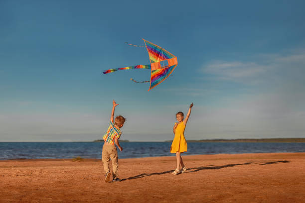 Two children play with a bright kite on the beach on a sunny day in summer.