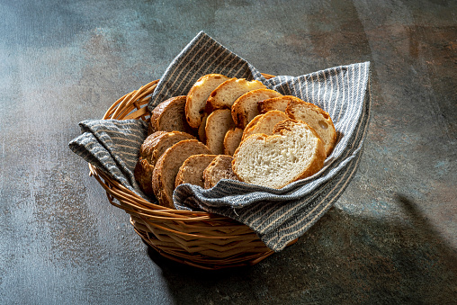 Slices of white bread with whole grain bread in a small wicker basket on colored background.