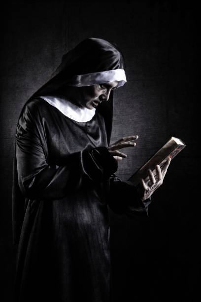 Horror Scene of a Possessed nun Woman with scripture bible Horror Scene of a Possessed nun Woman with scripture bible textbook and look at camera ghost halloween in dark room angry nun stock pictures, royalty-free photos & images