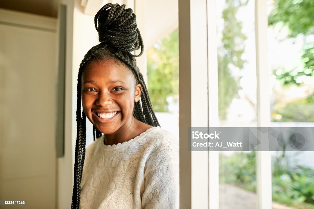 Cheerful african teenage girl coming in her house Portrait of a cheerful african teenage girl with braided hairstyle walking in the house from the entrance door Teenager Stock Photo