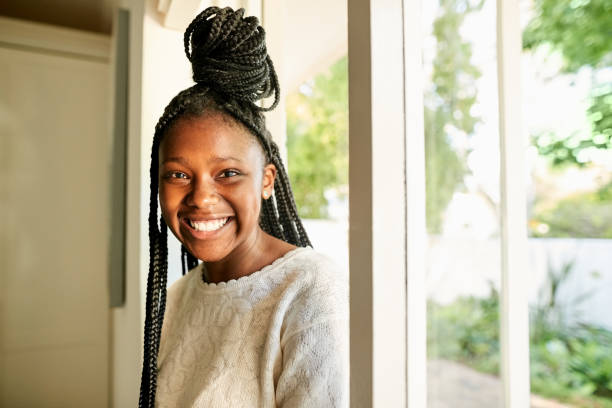 Cheerful african teenage girl coming in her house Portrait of a cheerful african teenage girl with braided hairstyle walking in the house from the entrance door cute 15 year old girls stock pictures, royalty-free photos & images