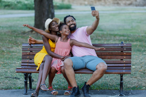 família alegre da etnia afro-americana está se divertindo no parque durante um dia de verão e tirando selfie foto. - grass summer day sunset - fotografias e filmes do acervo