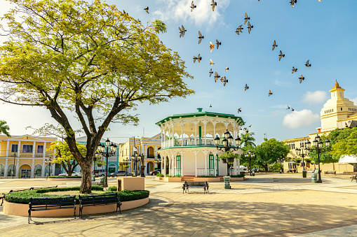 Flying birds in the sky of the Central Park in Puerto Plata, Independence Square, Plaza de Independencia, and a catholic church in the downtown