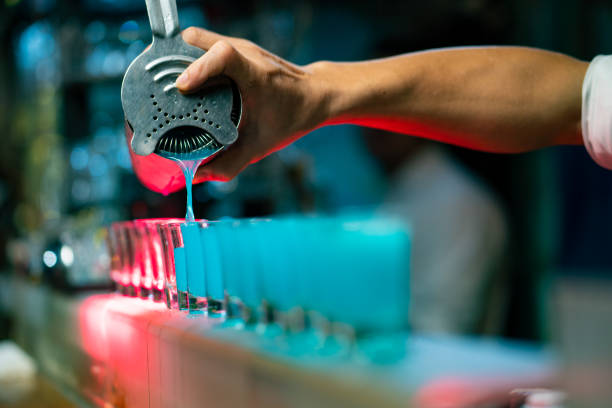istock Male bartender pouring mixed blue alcoholic cocktail drink from cocktail shaker into shot glass on bar counter. 1333666426