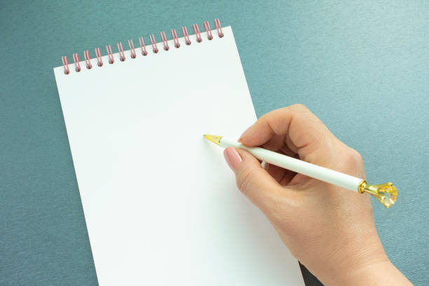 istock The hand of a woman holding a pen in an empty notebook. 1333672190