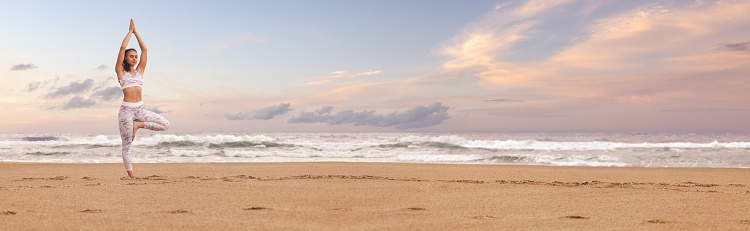 Young woman practicing yoga on the sea beach. Wide panoramic horizontal design with copy space