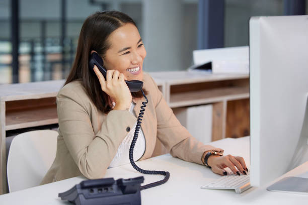 Shot of a young woman using a telephone and computer in a modern office You've called the right company using phone stock pictures, royalty-free photos & images