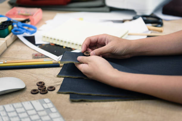 istock Hands of female tailor while compare the shirt buttons for maching fabric on table at cutting dressmaker studio, Cutting and design concept. Very shallow focus point at shirt buttons. 1333685946