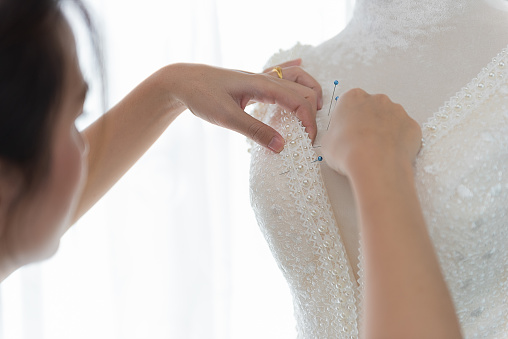 Designer woman's hands pin the Lace fabric on wedding dress at tailor shop. Body of bride. Sewing workshop, Closeup shot.
