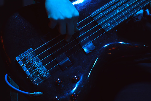The bass player plays on black five-string bass guitar in the spotlight. Selective focus