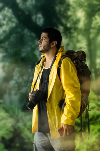 Photo of Adult tourist man exploring green tropical jungle wet with his backpack and a camera