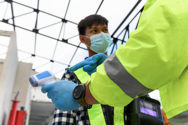 istock Labour Screening, Construction foreman wearing protective face mask pointing measurement results of body temperature of welder worker in an Infrared Thermometer during coronavirus COVID-19 Pandemic 1333691181